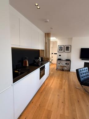 Recently renovated kitchen with white cabinetry, black splashback and oak flooring