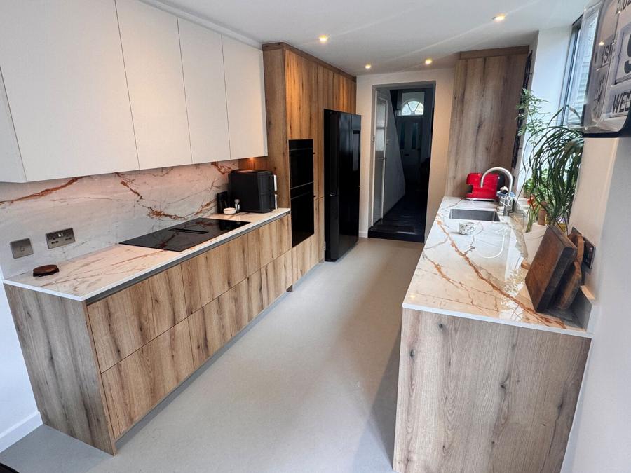 Both runs of the Bermondsey kitchen, with white wall units above wood bases and dark integrated appliances