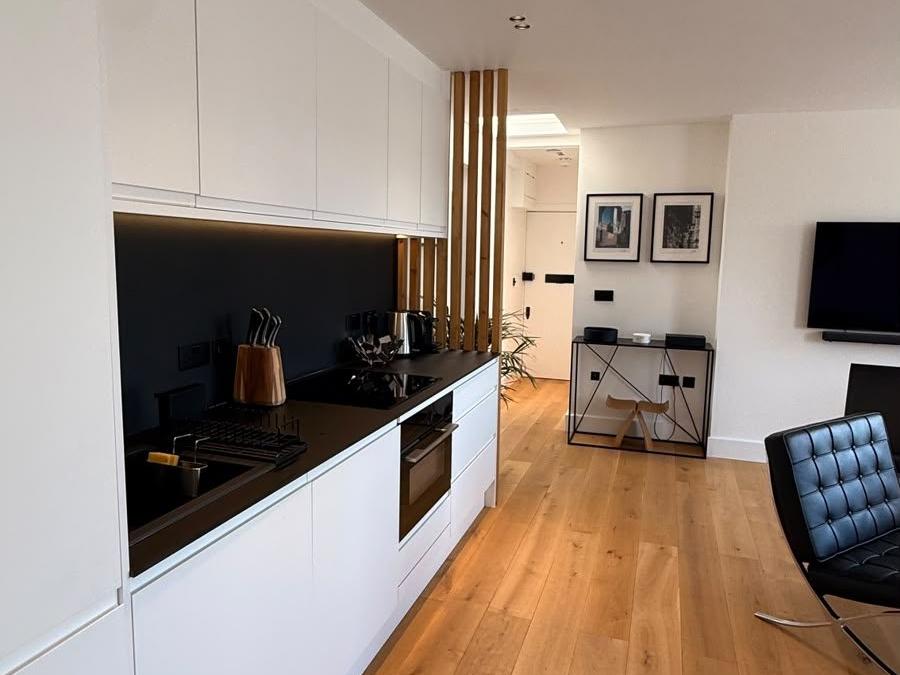 Marylebone kitchen after renovation, with white cabinetry, black splashback and oak floor