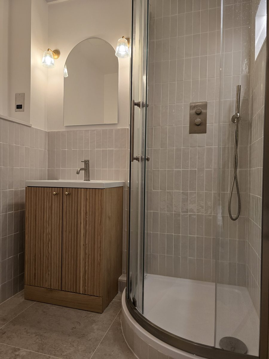 Recently renovated bathroom in Rotherhithe with a curved glass shower enclosure, arched mirror and oak vanity